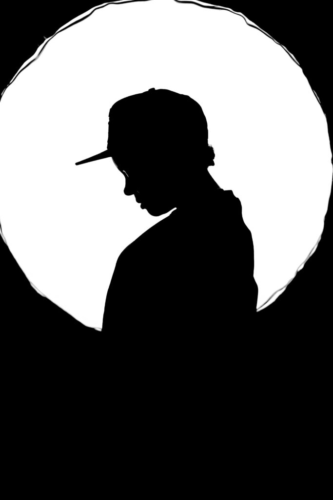 Artistic silhouette of a person with cap against a glowing full moon backdrop.